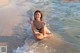 A woman in a bikini sitting in the water at the beach.