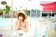 A woman in a straw hat sitting on a bench by a pool.