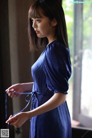 A woman in a blue dress standing by a window.