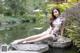 A woman sitting on a rock by a pond.